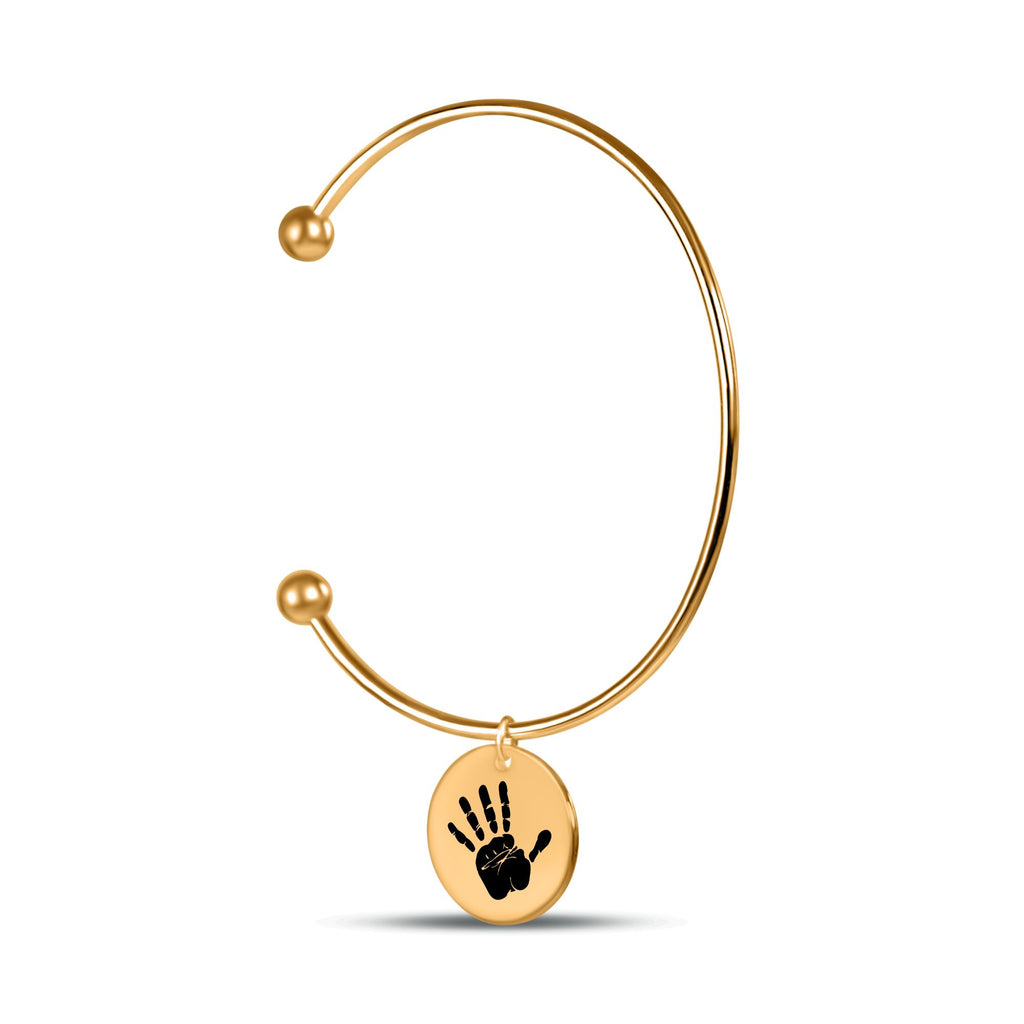 Filigraner goldener offene-Armreif mit rundem Anhänger und schwarzem Baby-Handabdruck auf weißem Hintergrund