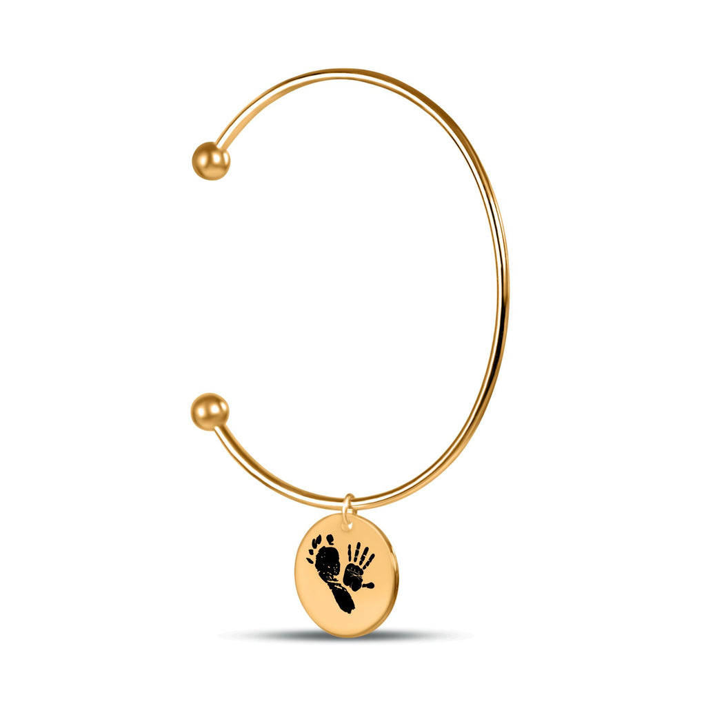 Filigraner vergoldeter Cuff-Armreif mit rundem Anhänger und Baby-Hand- und Fußabdruck auf weißem Hintergrund