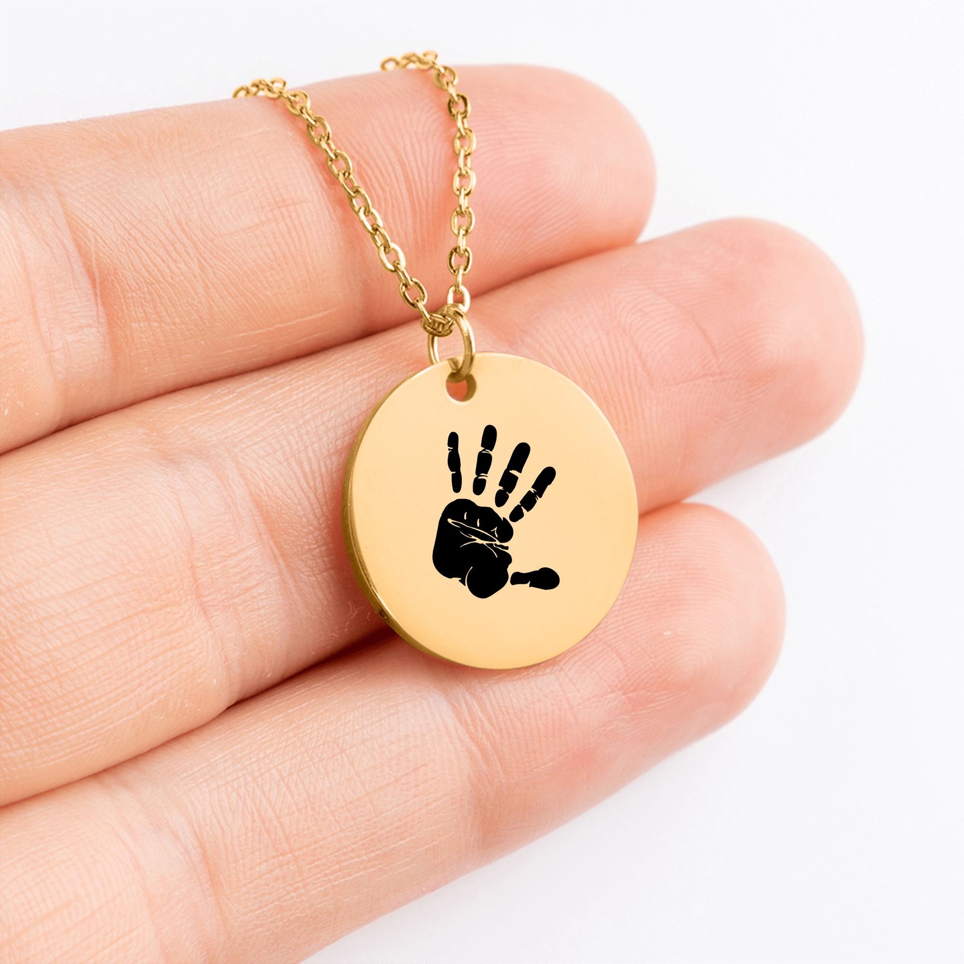 Detailaufnahme eines runden vergoldeten Anhängers an einer Gliederkette, der auf Fingerspitzen präsentiert wird und eine detaillierte Handabdruck-Gravur zeigt
